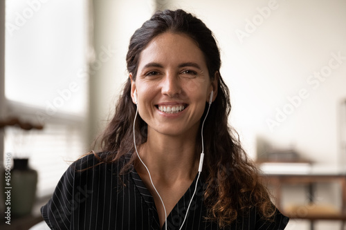 Tableau sur toile Head shot of happy Latin woman with wire earphones looking at camera, talking, speaking, smiling at webcam
