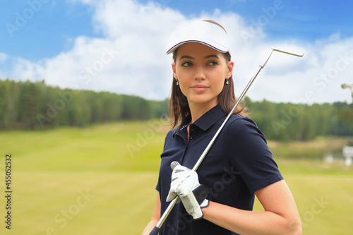 Professional female golfer holding golf club on field and looking away. Young woman standing on golf course on a sunny day.