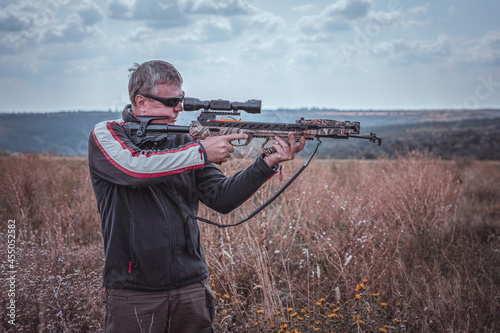 Fotografia, Obraz Hunter with a crossbow takes aim, half-length plan on the background of nature
