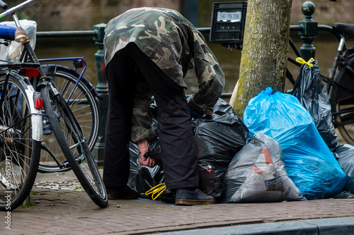 Photography A man searches for deposit bottles in garbage bags along a canal in Amsterdam, N