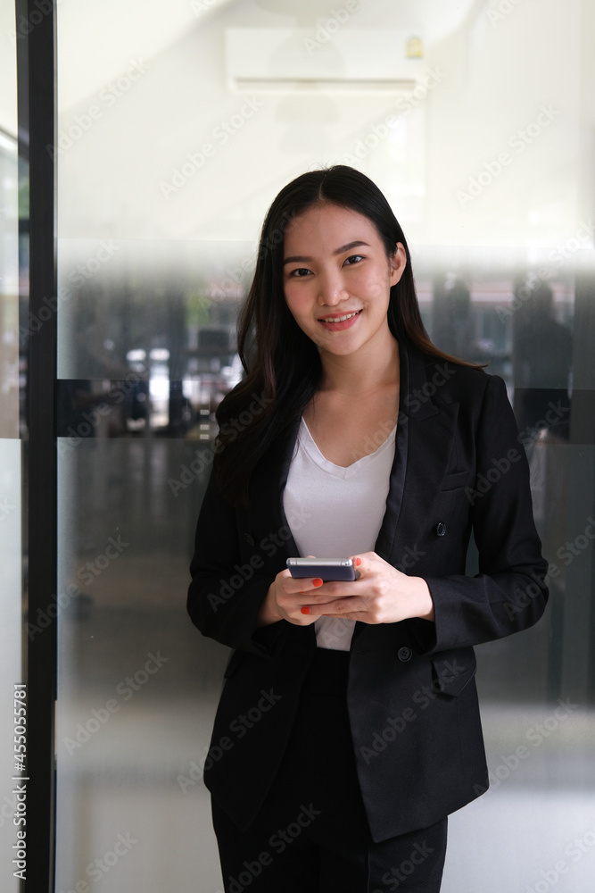 Portrait with beautiful Asian office woman holding smart phone and standing in front of glasses door. Portrait with beautiful Asian office woman holding smart phone and standing in front of glasses door.