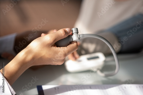 Hand of doctor using sphygmomanometer for checking blood pressure. Physician examining patient with complaints on hypertension, high pulse rate, rapid heart beating. Medical care, checlup. Close up