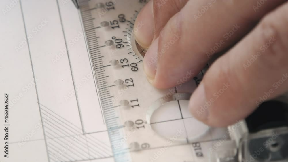 Close-up of a pencil draws the line on white paper using a transparent ruler. An engineer (architect, designer, or anybody else) using a ruler for sketch drawing or plane. Close-up of a pencil draws the line on white paper using a transparent ruler. An engineer (architect, designer, or anybody else) using a ruler for sketch drawing or plane.