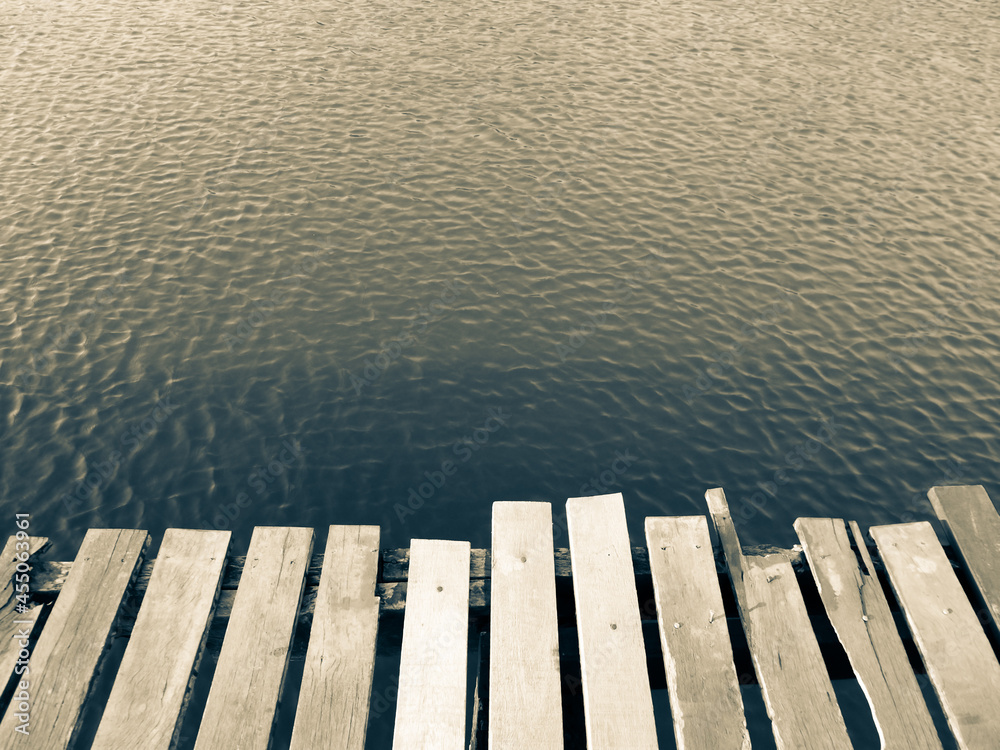 Fototapeta premium Mole (pier) on the lake. Wooden bridge in forest in spring time with blue lake. Lake for fishing with pier. Dark and Foggy lake nature beautiful background
