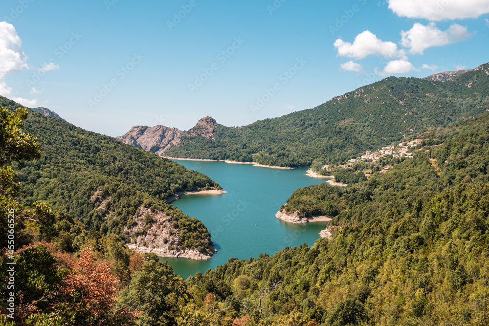 The dam wall at Lac de Tolla in Corsica surrounded by rocky cliffs and pine forest with mountains in the distance