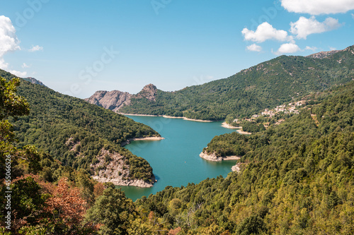 Fototapeta Naklejka Na Ścianę i Meble -  The dam wall at Lac de Tolla in Corsica surrounded by rocky cliffs and pine forest with mountains in the distance