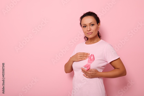 African American woman puts hands around pink ribbon on her pink T Shirt, for breast cancer campaign, supporting Breast Cancer Awareness. Concept of 1 st October Pink Month and women's health care