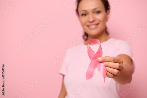 Blurred smiling African woman in pink t-shirt holding satin ribbon in her hand. Breast and abdominal cancer awareness, October Pink day on colored background, copy space. Breast cancer support concept