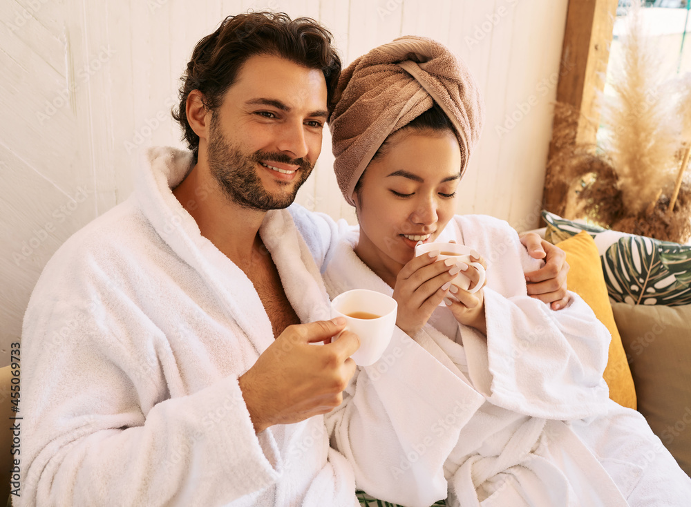 Loving young couple in white bathrobes spending a weekend at a spa and enjoying wellness tea. Resort and spa salon - obrazy, fototapety, plakaty 