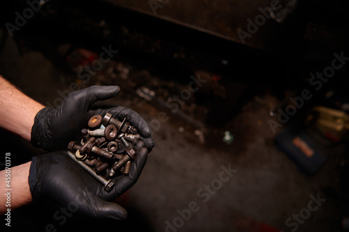 Car mechanic holding various black metal screws