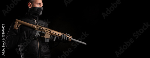 Fotografía A man in dark clothes holds an automatic carbine in his hands