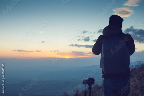 the photographer on the mountain takes a photo at sunset © S...