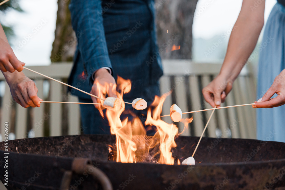 Fototapeta premium People cooking marshmallows on sticks over a flaming fire pit (no visible faces)