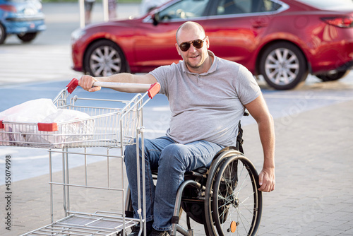 Disabled man in wheelchair pushing cart in front of himself at supermarket parking © romaset