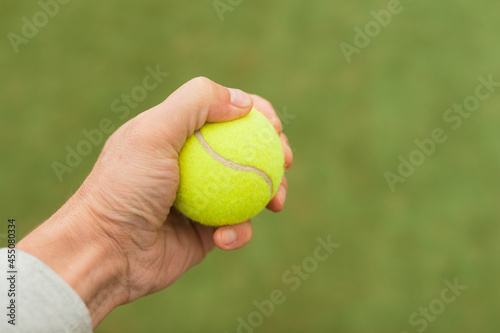The tennis player squeezes the tennis ball firmly during the game before serving.