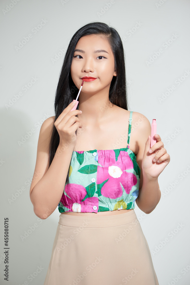 beautiful asian girl appying lip gloss on lips isolated on white.
