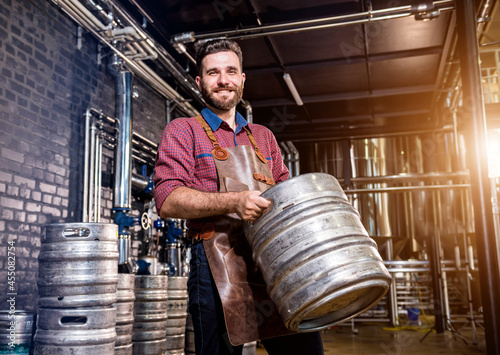 Obraz na płótnie Young male brewer in leather apron holds barrel with craft beer at modern brewer