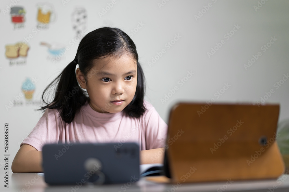 Asian child student or kid girl smiling learn from home school or people study online on computer tablet and video call learning on smartphone with happy enjoy to vocabulary english words in classroom Asian child student or kid girl smiling learn from home school or people study online on computer tablet and video call learning on smartphone with happy enjoy to vocabulary english words in classroom