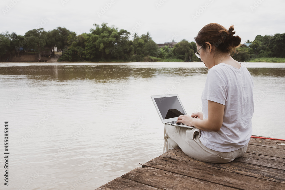 asian adult woman using computer to work remotely from riverside of rural area