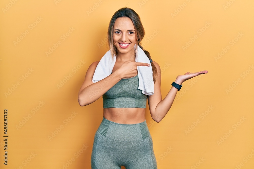 Beautiful hispanic woman wearing sportswear and towel amazed and smiling to the camera while presenting with hand and pointing with finger. Beautiful hispanic woman wearing sportswear and towel amazed and smiling to the camera while presenting with hand and pointing with finger.