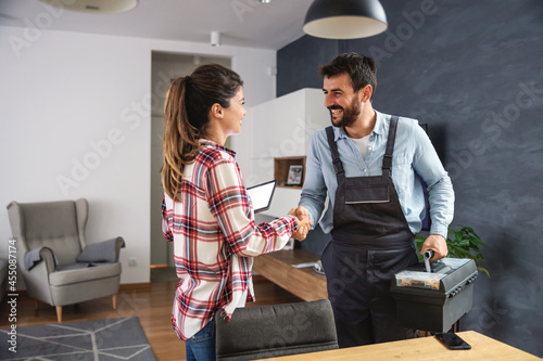 Happy woman shaking hands with repairman. Home interior. photo