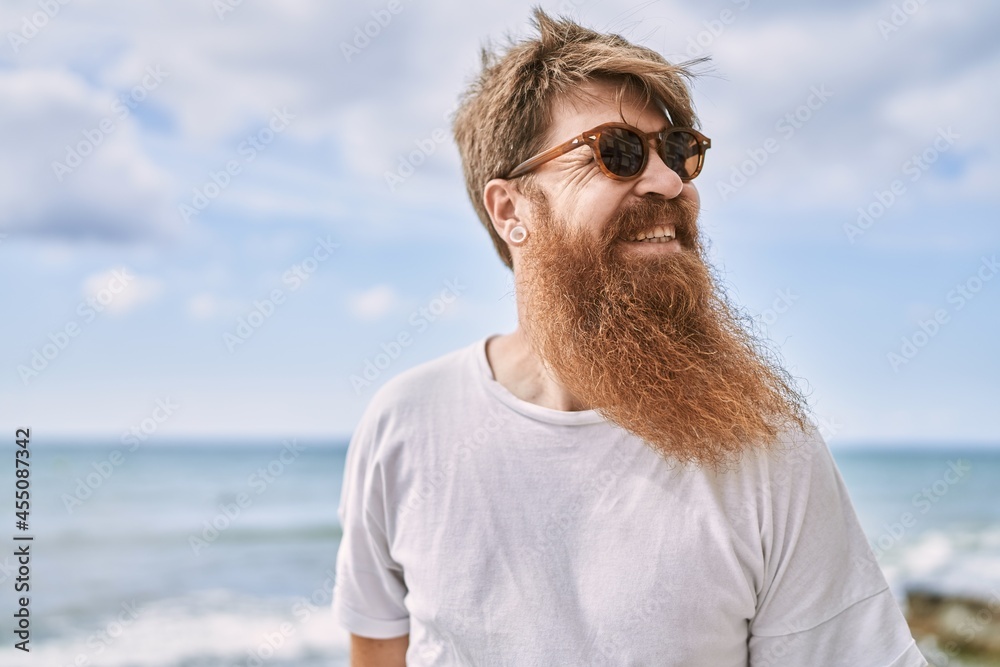Young redhead tourist man smiling happy standing at the beach. Young redhead tourist man smiling happy standing at the beach.