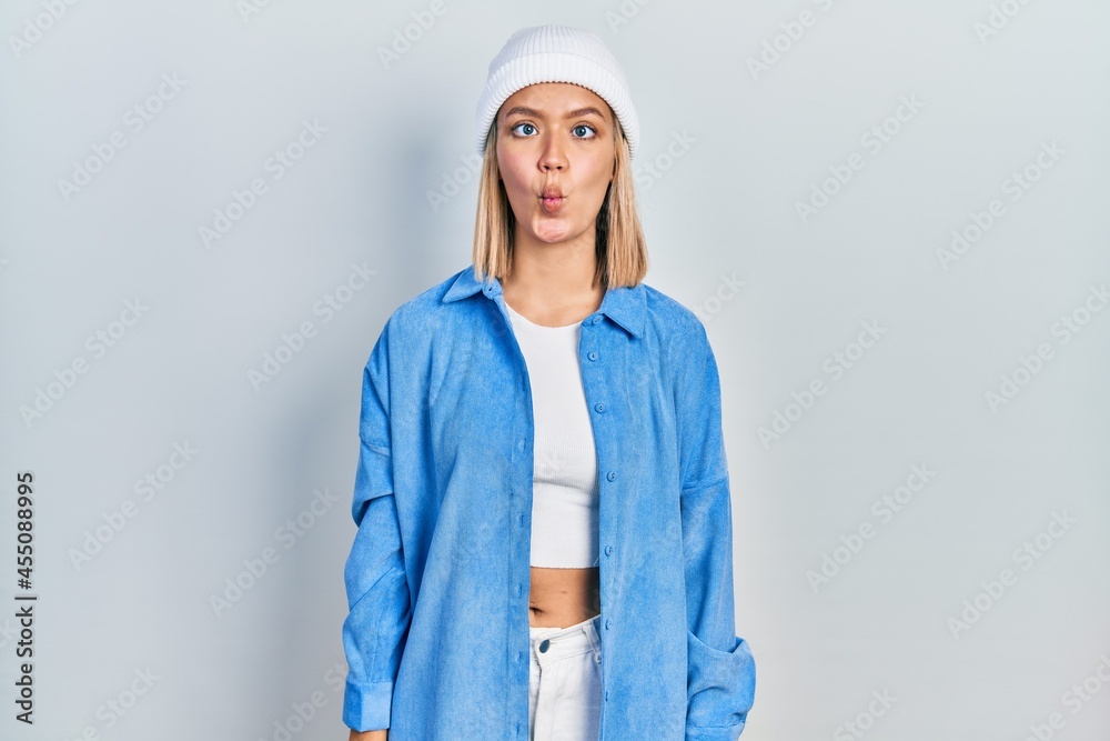 Fototapeta premium Beautiful blonde woman wearing wool hat making fish face with lips, crazy and comical gesture. funny expression.