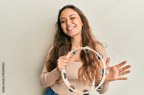 Obraz na plátně Young hispanic girl playing tambourine looking positive and happy standing and s