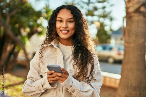 Young latin woman smiling happy using smartphone at the city.