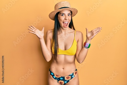 Young hispanic woman wearing bikini and summer hat celebrating crazy and amazed for success with arms raised and open eyes screaming excited. winner concept