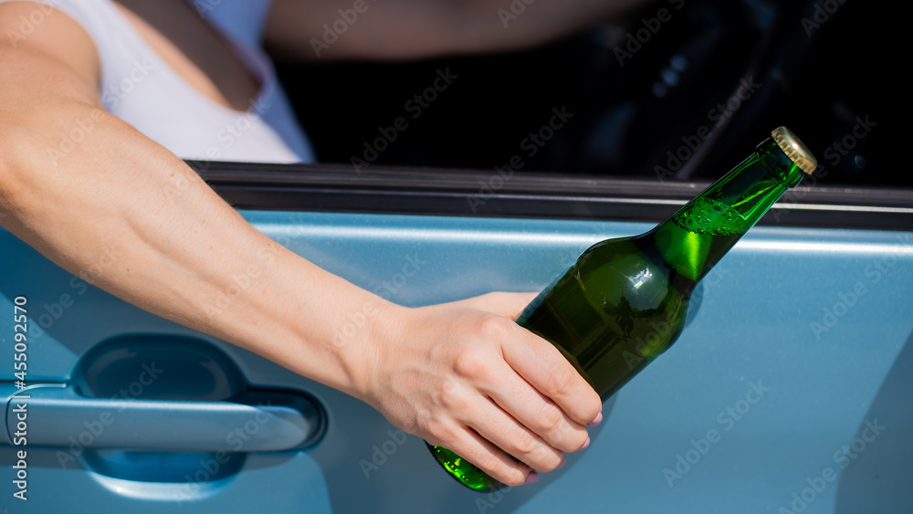 A faceless woman is drinking a bottle of beer while driving a car. Breaking the law and drinking alcohol while driving