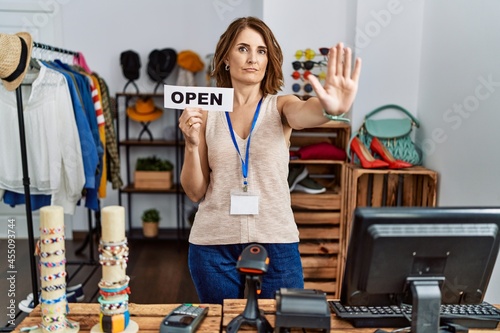 Fototapeta Naklejka Na Ścianę i Meble -  Middle age woman holding banner with open text at retail shop with open hand doing stop sign with serious and confident expression, defense gesture