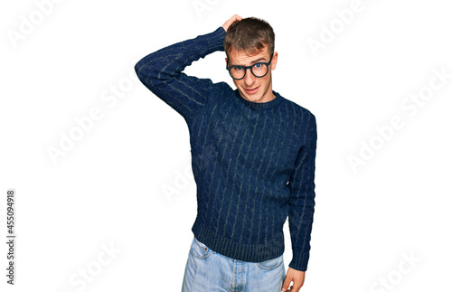 Young blond man wearing casual clothes and glasses confuse and wonder about question. uncertain with doubt, thinking with hand on head. pensive concept.