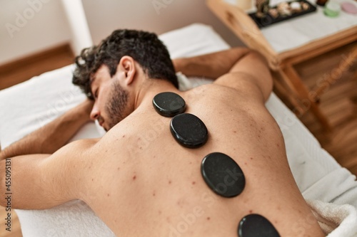 Man reciving back massage with black stones at beauty center.