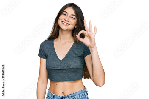 Young beautiful teen girl wearing casual crop top t shirt smiling positive doing ok sign with hand and fingers. successful expression.