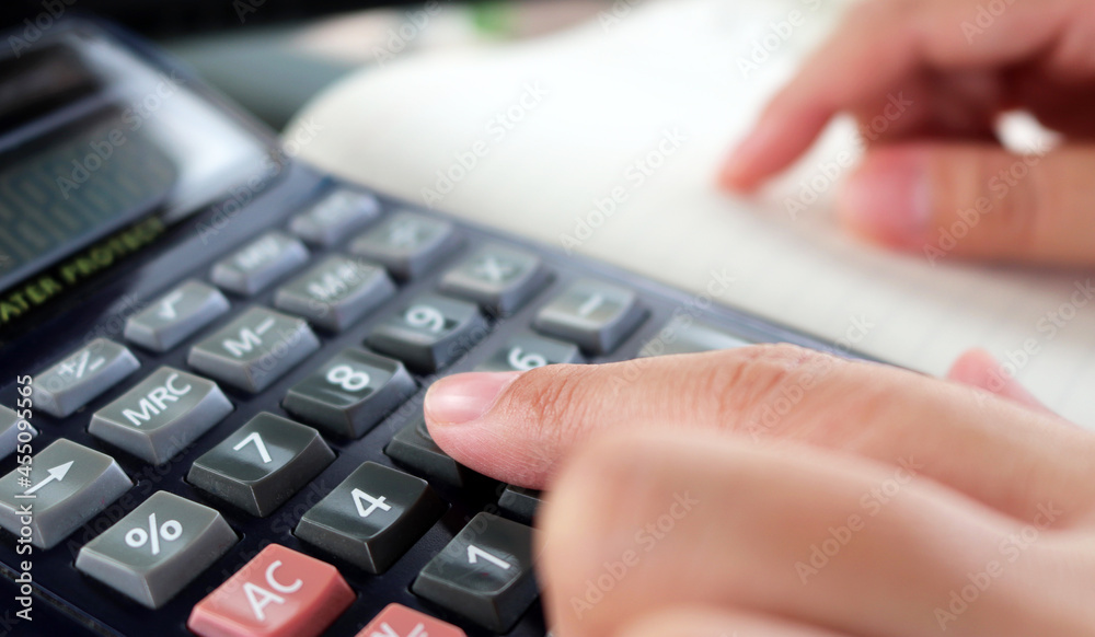 Woman works on calculator to convey the concepts of tax season and monthly expenses Woman works on calculator to convey the concepts of tax season and monthly expenses