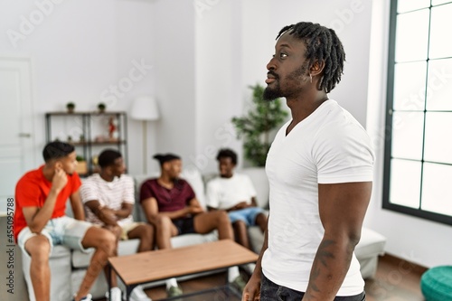 Young african man with friends at the living room looking to side, relax profile pose with natural face with confident smile.