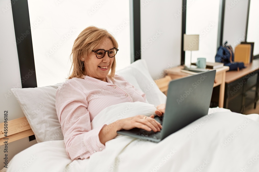 Middle age blonde woman smiling happy using laptop lying on the bed at home. Middle age blonde woman smiling happy using laptop lying on the bed at home.