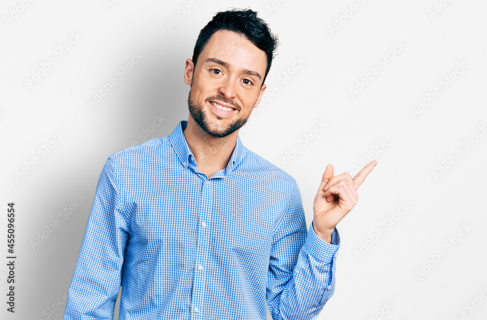 Hispanic man with beard wearing casual business shirt with a big smile on face, pointing with hand and finger to the side looking at the camera. Hispanic man with beard wearing casual business shirt with a big smile on face, pointing with hand and finger to the side looking at the camera.