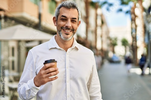 Middle age grey-haired man smiling happy drinking coffee at the city.