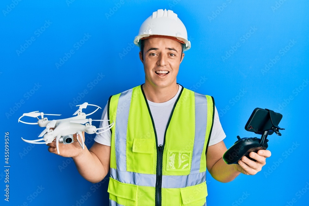 Handsome young man wearing safety hard using drone and control celebrating crazy and amazed for success with open eyes screaming excited. Handsome young man wearing safety hard using drone and control celebrating crazy and amazed for success with open eyes screaming excited.