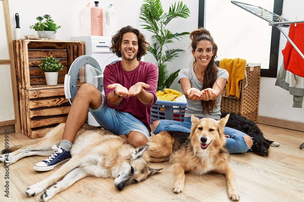 Young hispanic couple doing laundry with dogs smiling with hands palms together receiving or giving gesture. hold and protection