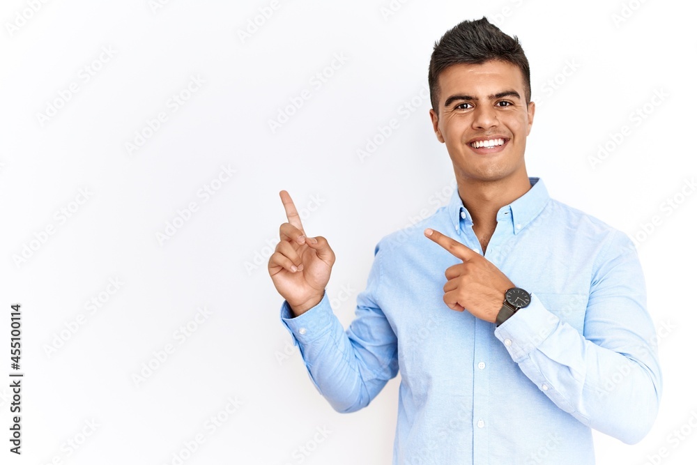 Young hispanic man wearing business shirt standing over isolated background smiling and looking at the camera pointing with two hands and fingers to the side. Young hispanic man wearing business shirt standing over isolated background smiling and looking at the camera pointing with two hands and fingers to the side.