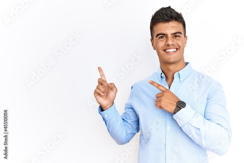 Young hispanic man wearing business shirt standing over isolated background smiling and looking at the camera pointing with two hands and fingers to the side.