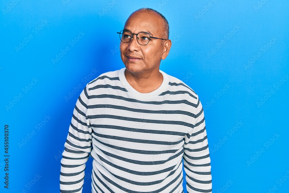 Middle age latin man wearing casual clothes and glasses looking away to side with smile on face, natural expression. laughing confident.