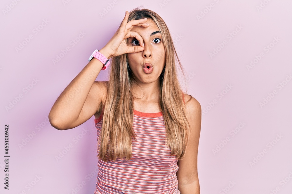 Fototapeta premium Beautiful hispanic woman wearing casual summer t shirt doing ok gesture shocked with surprised face, eye looking through fingers. unbelieving expression.