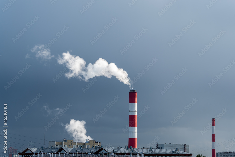 Thermal power plant cooling towers above the rooftops of city houses against the backdrop of a dark storm cloud.