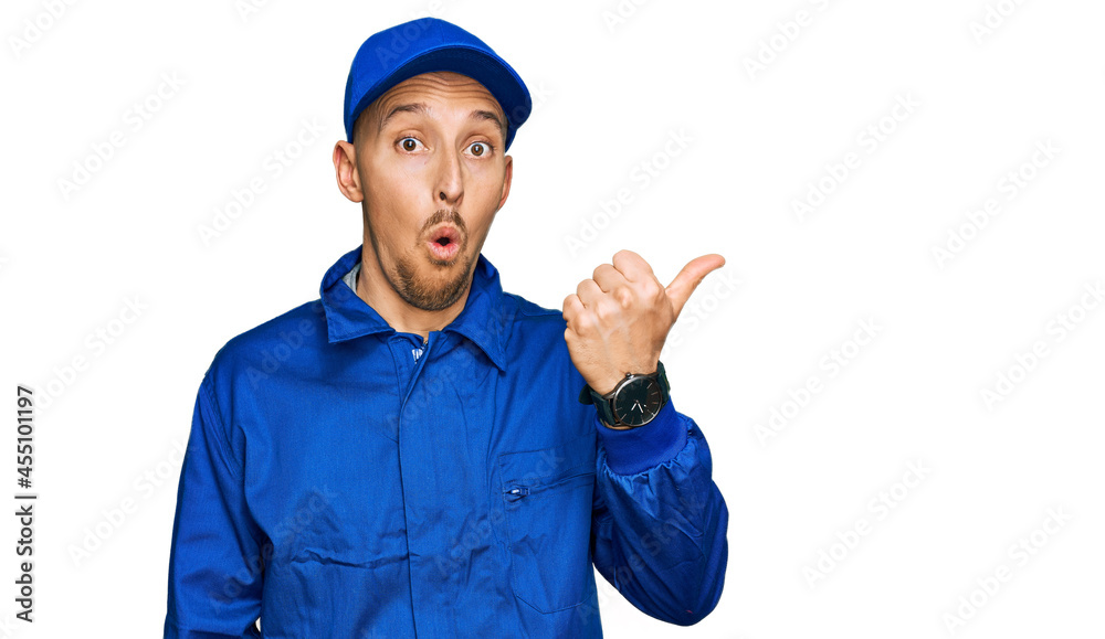 Bald man with beard wearing builder jumpsuit uniform surprised pointing with hand finger to the side, open mouth amazed expression. Bald man with beard wearing builder jumpsuit uniform surprised pointing with hand finger to the side, open mouth amazed expression.