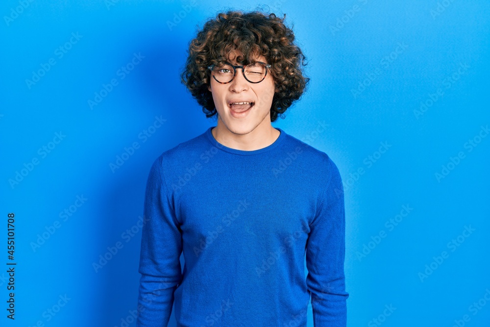 Handsome young man wearing casual clothes and glasses winking looking at the camera with sexy expression, cheerful and happy face. Handsome young man wearing casual clothes and glasses winking looking at the camera with sexy expression, cheerful and happy face.