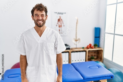 Young handsome physiotherapist man working at pain recovery clinic winking looking at the camera with sexy expression  cheerful and happy face.